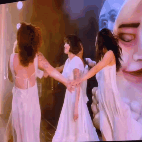 A Group Of Women In White Dresses Are Holding Hands GIF
