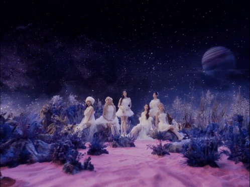 A Group Of Women In White Dresses Are Sitting In A Pink Field GIF