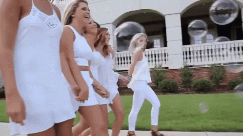 A Group Of Women In White Dresses Are Walking Down The Street . GIF