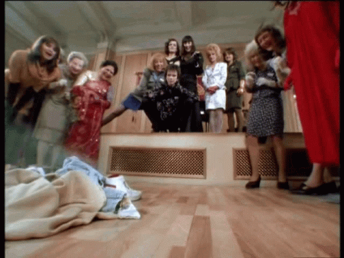 A Group Of Women Standing Around A Man In A Room GIF