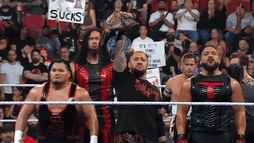 A Group Of Wrestlers Are Holding Up A Sign That Says Sucks GIF