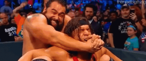 A Group Of Wrestlers Are Hugging Each Other On A Wrestling Ring In Front Of A Crowd . GIF