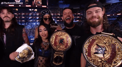 A Group Of Wrestlers Are Posing For A Picture And One Of Them Is Holding A Wwe World Heavyweight Championship Belt GIF