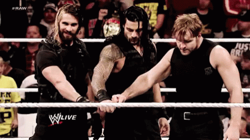 A Group Of Wrestlers Are Standing In A Ring Holding Hands . GIF