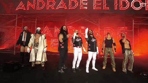 A Group Of Wrestlers Stand In Front Of A Sign That Says Andrade El Idol GIF