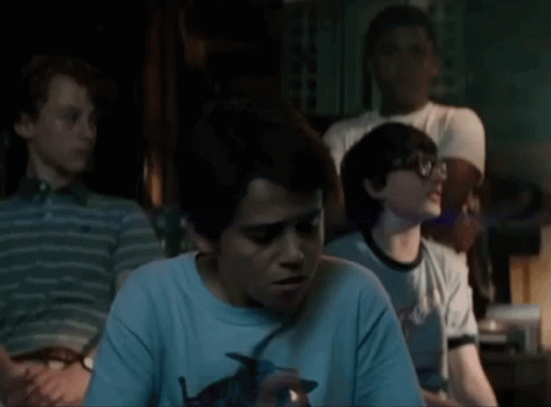 A Group Of Young Boys Are Sitting In A Dark Room And One Of Them Is Holding A Lighter . GIF