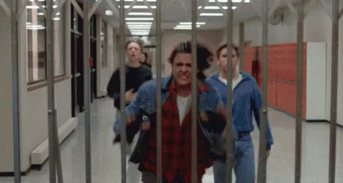 A Group Of Young Men Are Running Through A Hallway Behind A Fence . GIF