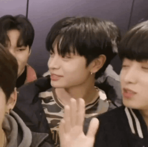 A Group Of Young Men Are Sitting Around A Table And One Of Them Is Waving His Hand . GIF