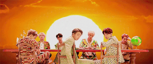 a group of young men are sitting around a table with a globe in front of a sunset .