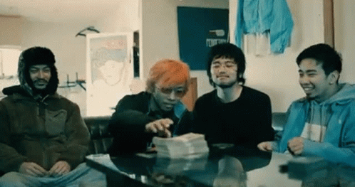 A Group Of Young Men Are Sitting Around A Table With A Pile Of Money . GIF