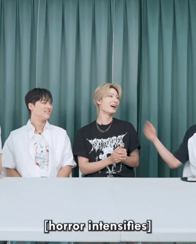 A Group Of Young Men Are Sitting At A Table And One Of Them Is Wearing A Black Shirt That Says " Horror Intensifies " GIF