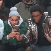 A Group Of Young Men Are Sitting In A Crowd Looking At Their Cell Phones . GIF