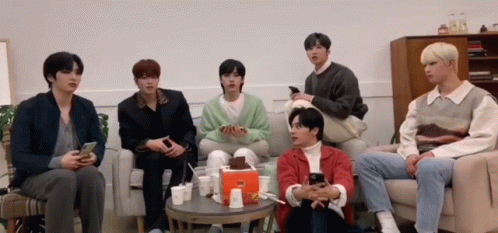 A Group Of Young Men Are Sitting On A Couch Looking At Their Cell Phones . GIF