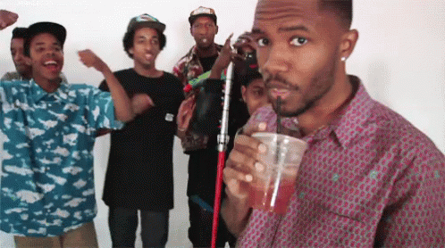 A Group Of Young Men Are Standing Around A Man Drinking A Drink Through A Straw GIF