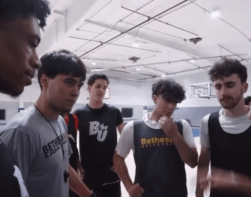 A Group Of Young Men Are Standing In A Gym And One Of Them Is Wearing A Shirt That Says Bethess University GIF