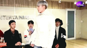A Group Of Young Men Are Standing In A Room With The Word Entertainment On The Wall Behind Them GIF