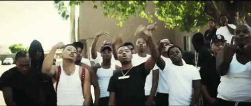 A Group Of Young Men Are Standing In Front Of A Building With Their Hands In The Air . GIF