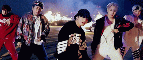 A Group Of Young Men Are Standing Next To Each Other In A Parking Lot In Front Of A Fire . GIF