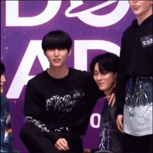 A Group Of Young Men Are Standing Next To Each Other In Front Of A Purple Sign . GIF