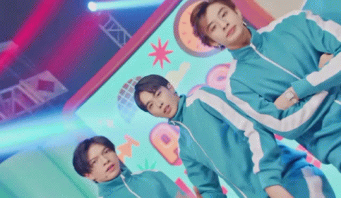 A Group Of Young Men Are Standing Next To Each Other On A Stage In Squid Game Costumes . GIF