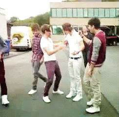 A Group Of Young Men Are Standing On A Sidewalk Talking To Each Other GIF