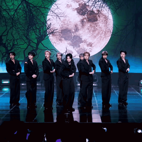 A Group Of Young Men Are Standing On A Stage In Front Of A Full Moon GIF