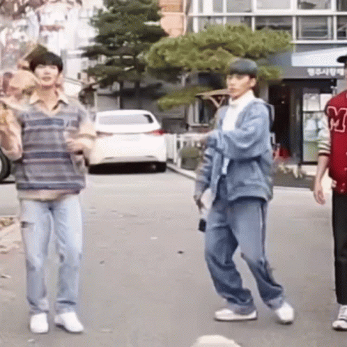 A Group Of Young Men Are Standing On A Street . GIF