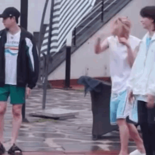 A Group Of Young Men Are Standing On A Wet Sidewalk . GIF