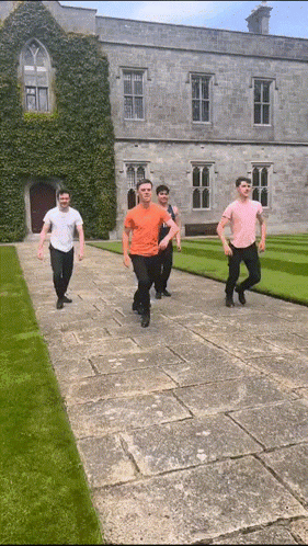 a group of young men are walking down a stone walkway in front of a large building