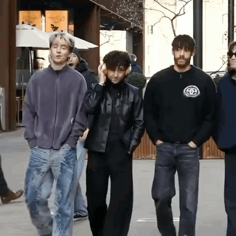 A Group Of Young Men Are Walking Down A Street And One Of Them Is Wearing Headphones GIF