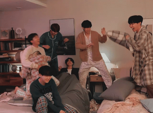 A Group Of Young Men In Pajamas Are Having A Pillow Fight In A Room GIF