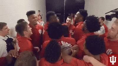 A Group Of Young Men In Red Shirts Are Hugging Each Other In A Room . GIF