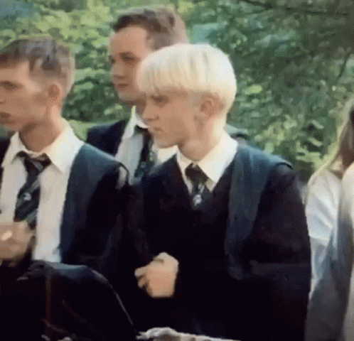 A Group Of Young Men In Suits And Ties Are Standing Next To Each Other In A Park . GIF
