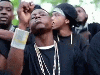 A Group Of Young Men Wearing Black Shirts And Pearl Necklaces Are Standing Next To Each Other . GIF