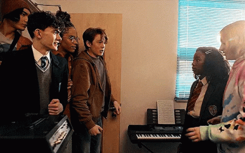 A Group Of Young People Are Standing Next To Each Other In A Room With A Piano . GIF