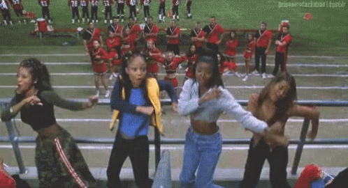 A Group Of Young Women Are Dancing In A Stadium While Cheerleaders Are Standing In The Background . GIF