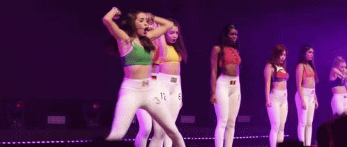 A Group Of Young Women Are Dancing On A Stage With Purple Lights . GIF