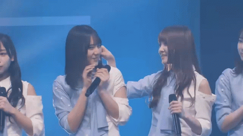 A Group Of Young Women Are Standing In Front Of A Blue Background And One Of Them Is Holding A Microphone GIF