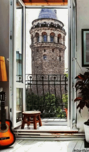 A Guitar Sits On The Floor In Front Of A Balcony With A View Of A Tower GIF