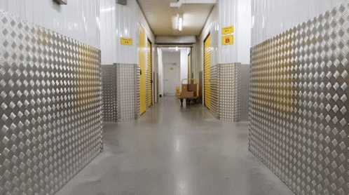 A Hallway With Metal Walls And A Yellow Sign That Says ' Warehouse ' On It GIF