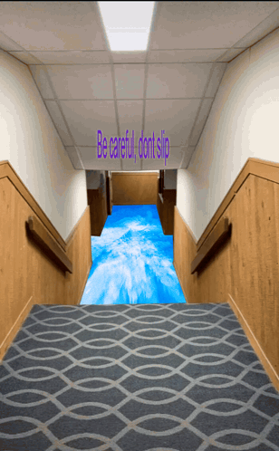 a hallway with stairs and a blue carpet that says be careful dont slip