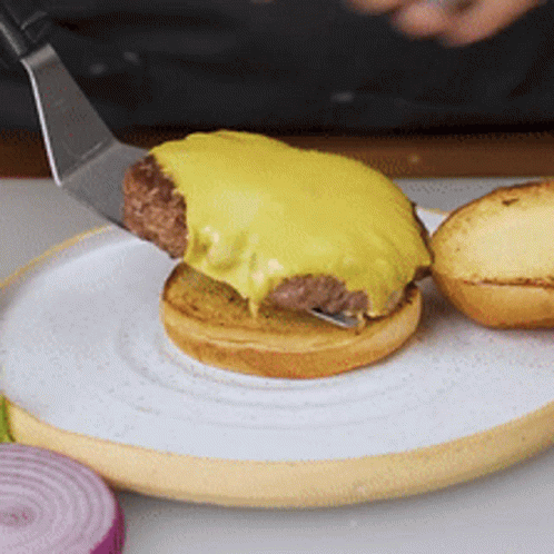 A Hamburger Is Being Served On A White Plate With A Spatula GIF