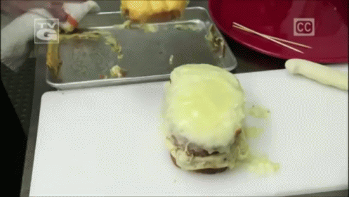 A Hamburger Is Sitting On A White Cutting Board With A Cc Logo On It GIF