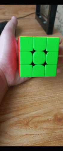 A Hand Is Holding A Green And Red Cube On A Wooden Table GIF