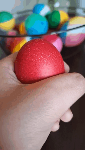 A Hand Is Holding A Red Ball In Front Of A Bowl Of Balls GIF