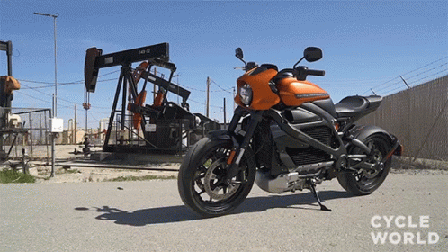 A Harley Davidson Motorcycle Is Parked On The Side Of The Road In Front Of An Oil Pump GIF
