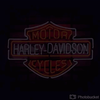 A Harley Davidson Neon Sign Is Lit Up On A Red Brick Wall . GIF