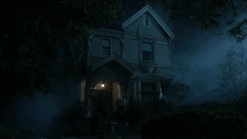 A Haunted House Is Lit Up At Night With Trees In The Foreground GIF