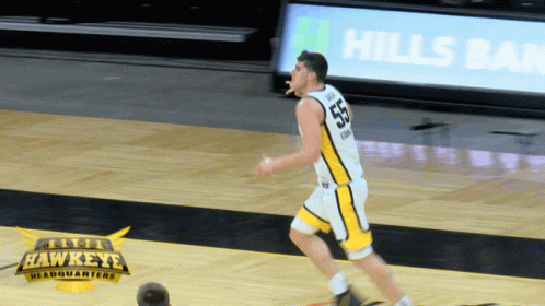 A Hawkeye Basketball Player Dribbles The Ball In Front Of An Advertisement For Hills Bank GIF