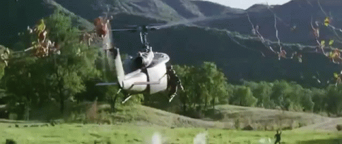 A Helicopter Is Flying Over A Grassy Field . GIF